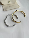 Two lune bracelets, one gold and one silver, on a light gray surface with a brand name card in the background