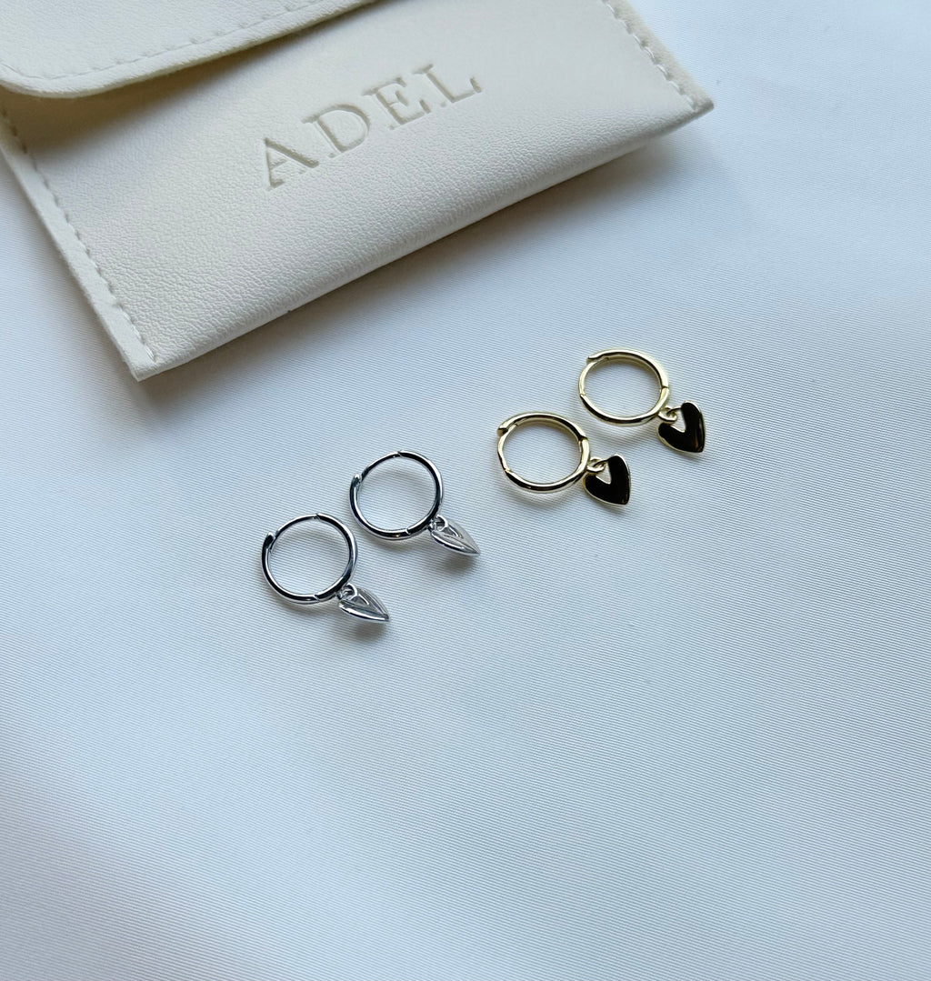 Two pairs of hoop earrings with leaf details on a light gray surface, with a beige jewelry pouch labeled 'ADEL' in the background.