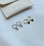 Two pairs of hoop earrings with leaf details on a light gray surface, with a beige jewelry pouch labeled 'ADEL' in the background.