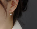 Heart-shaped silver earring worn by a person with a neutral background