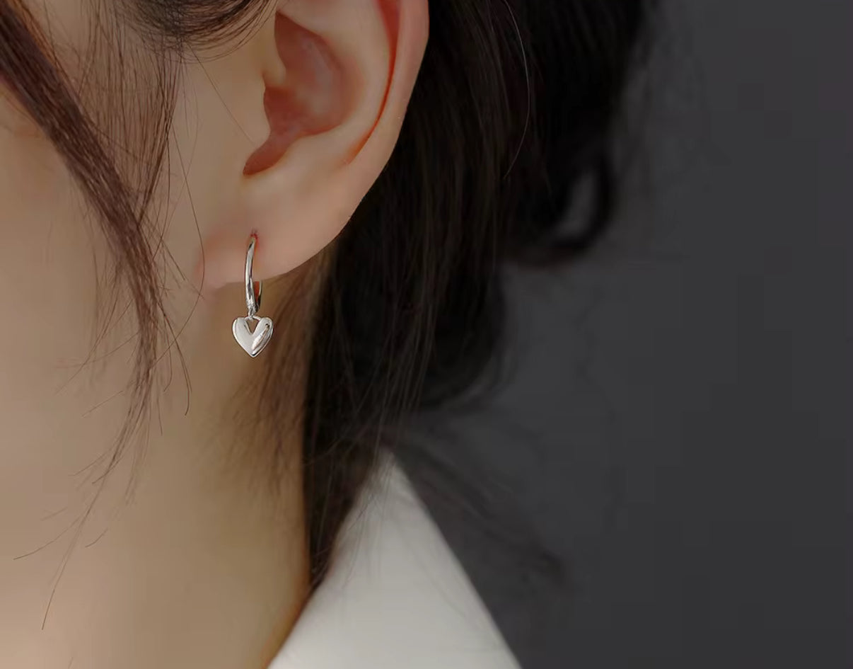 Heart-shaped silver earring worn by a person with a neutral background