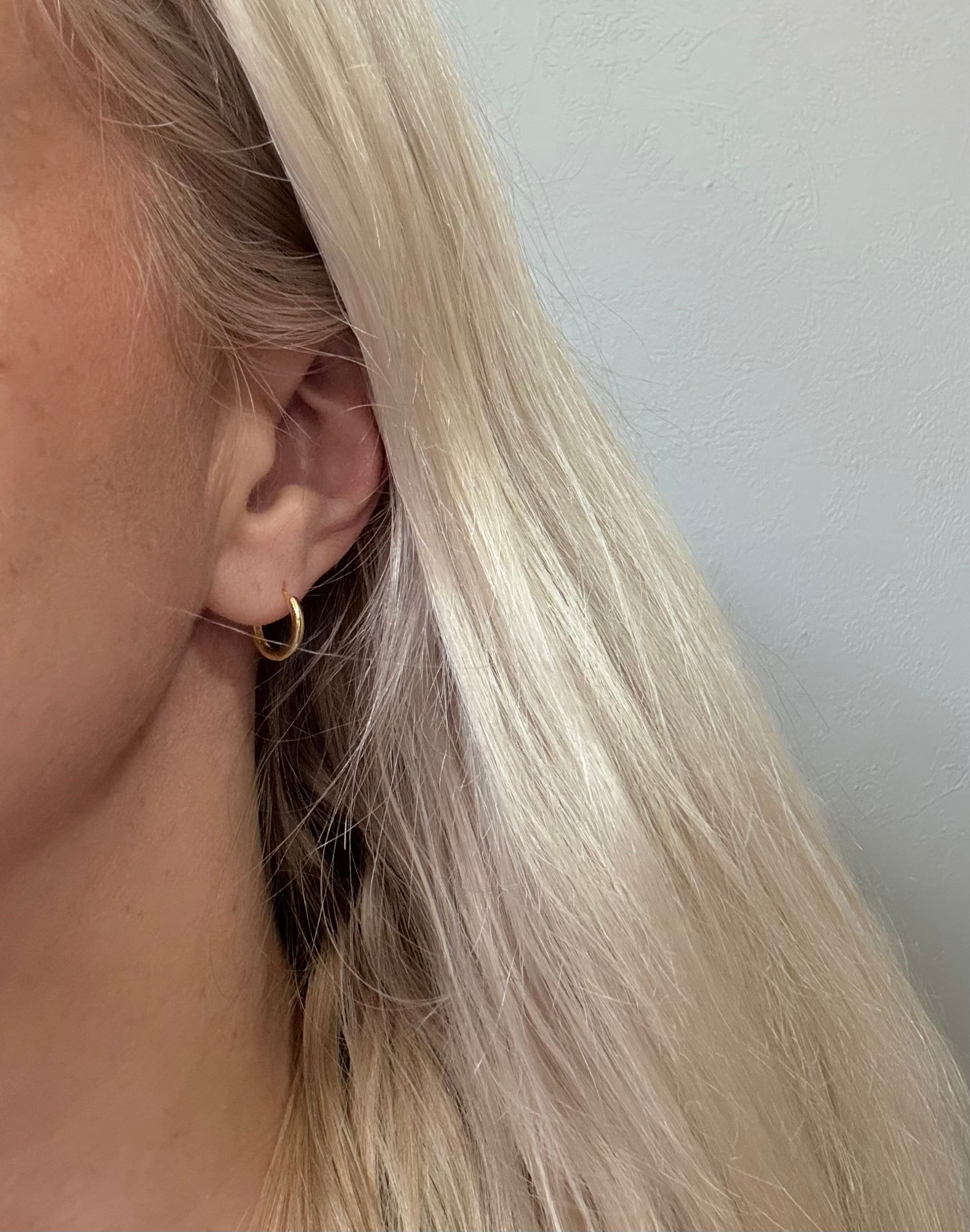 Close-up of an ear wearing a gold hoop earring with blonde hair.