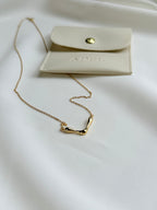 Gold necklace on a white surface with a beige card featuring 'ADEL' branding.