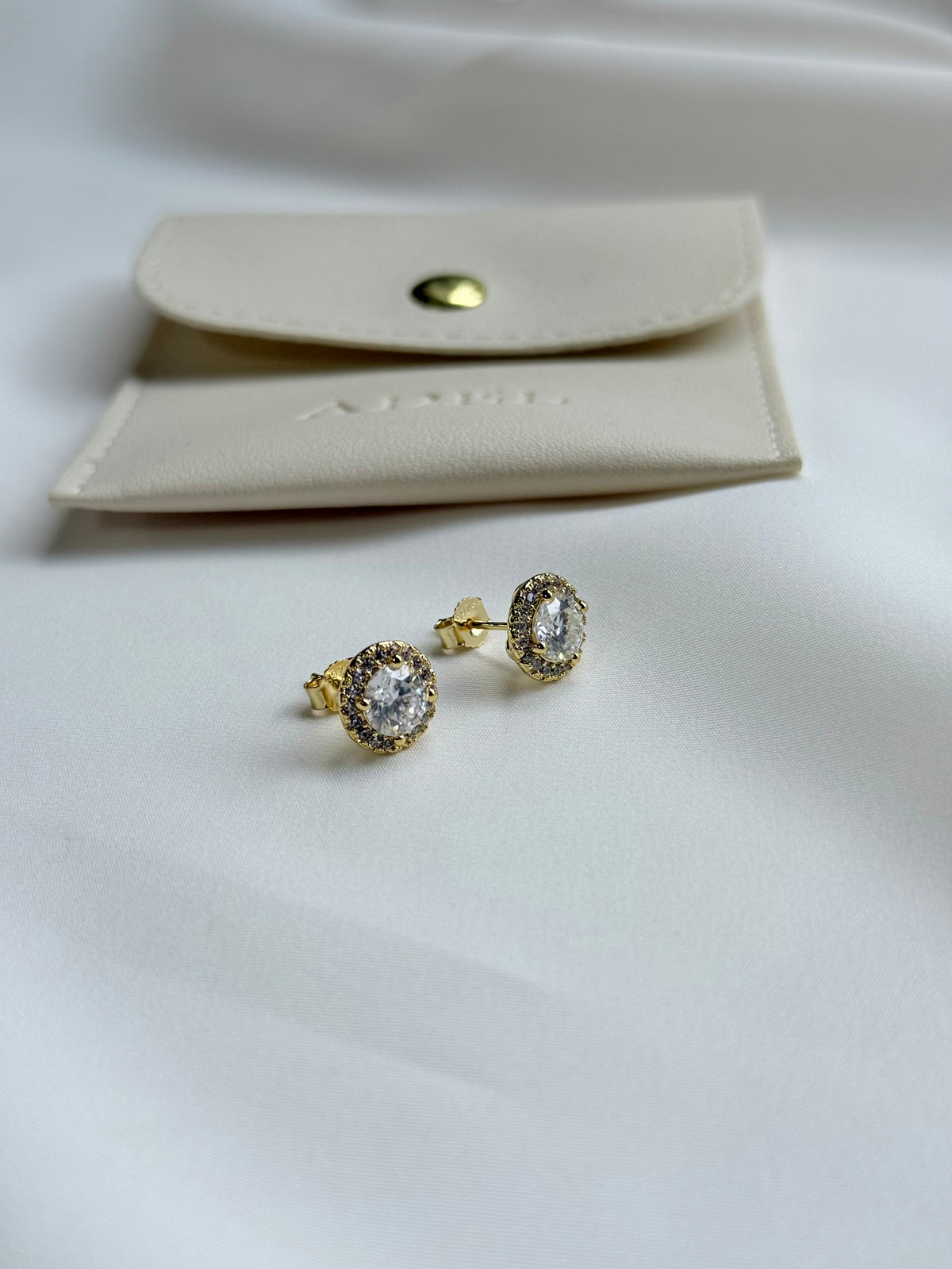 Gold earrings with moissanite on a white surface next to a beige jewelry pouch.
