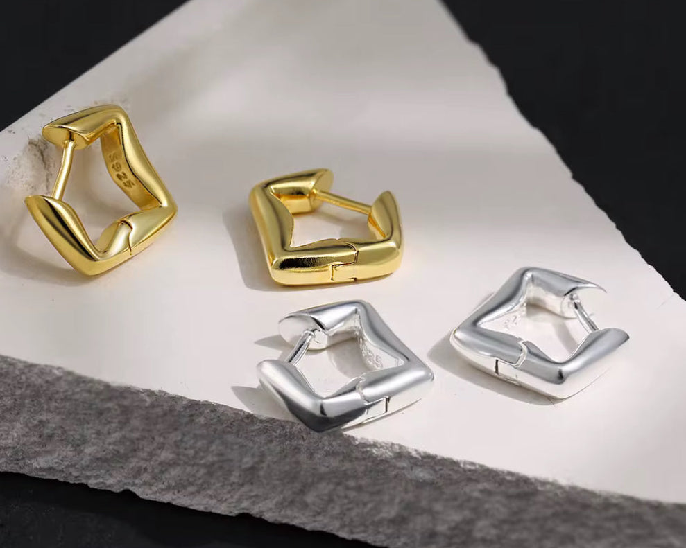 Gold and silver hoop earrings on a stone surface with a dark background