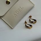 Gold hoop earrings next to a beige jewelry pouch with 'ADEL' branding on a light gray background