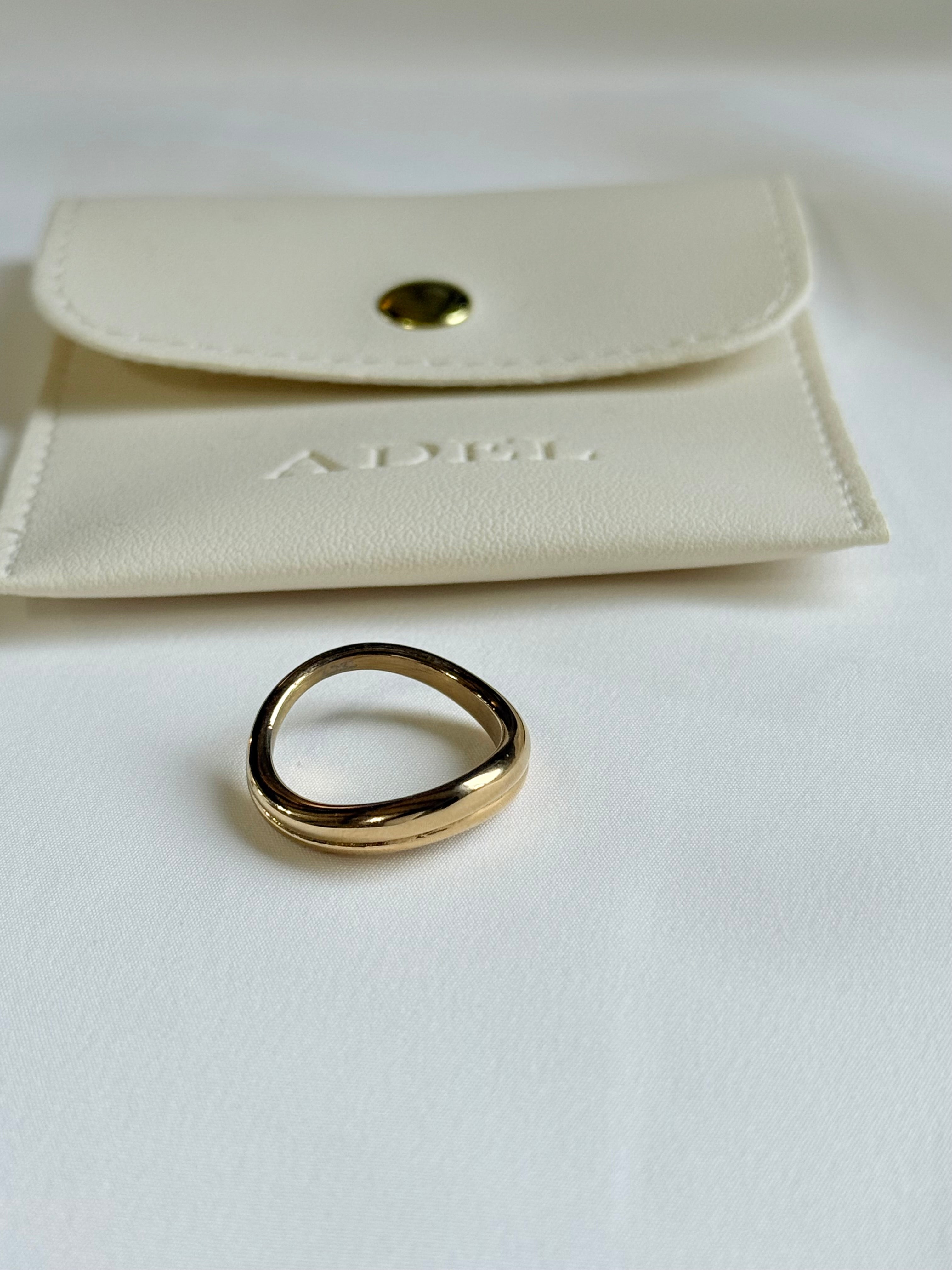 Gold ring on a white surface with a beige pouch in the background