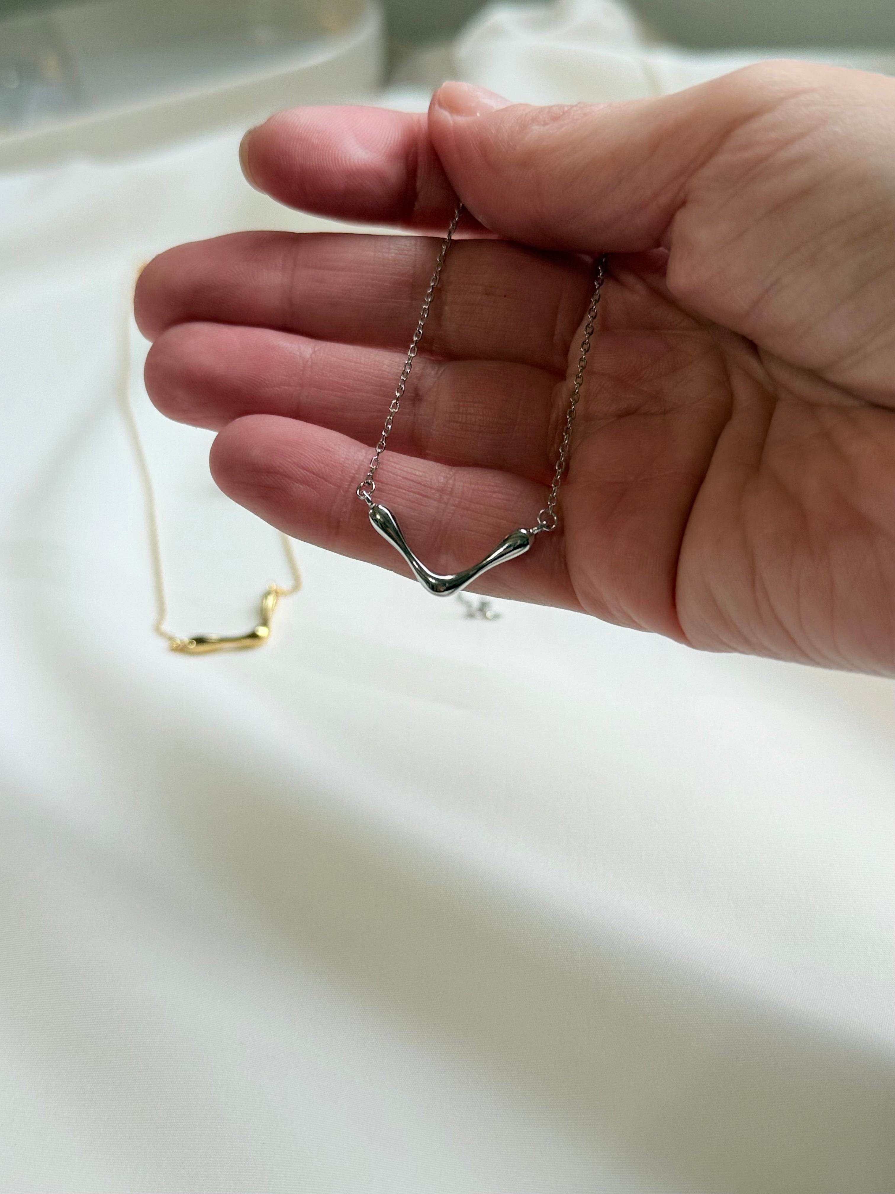 Hand holding a silver necklace with a V-shaped pendant on a light background