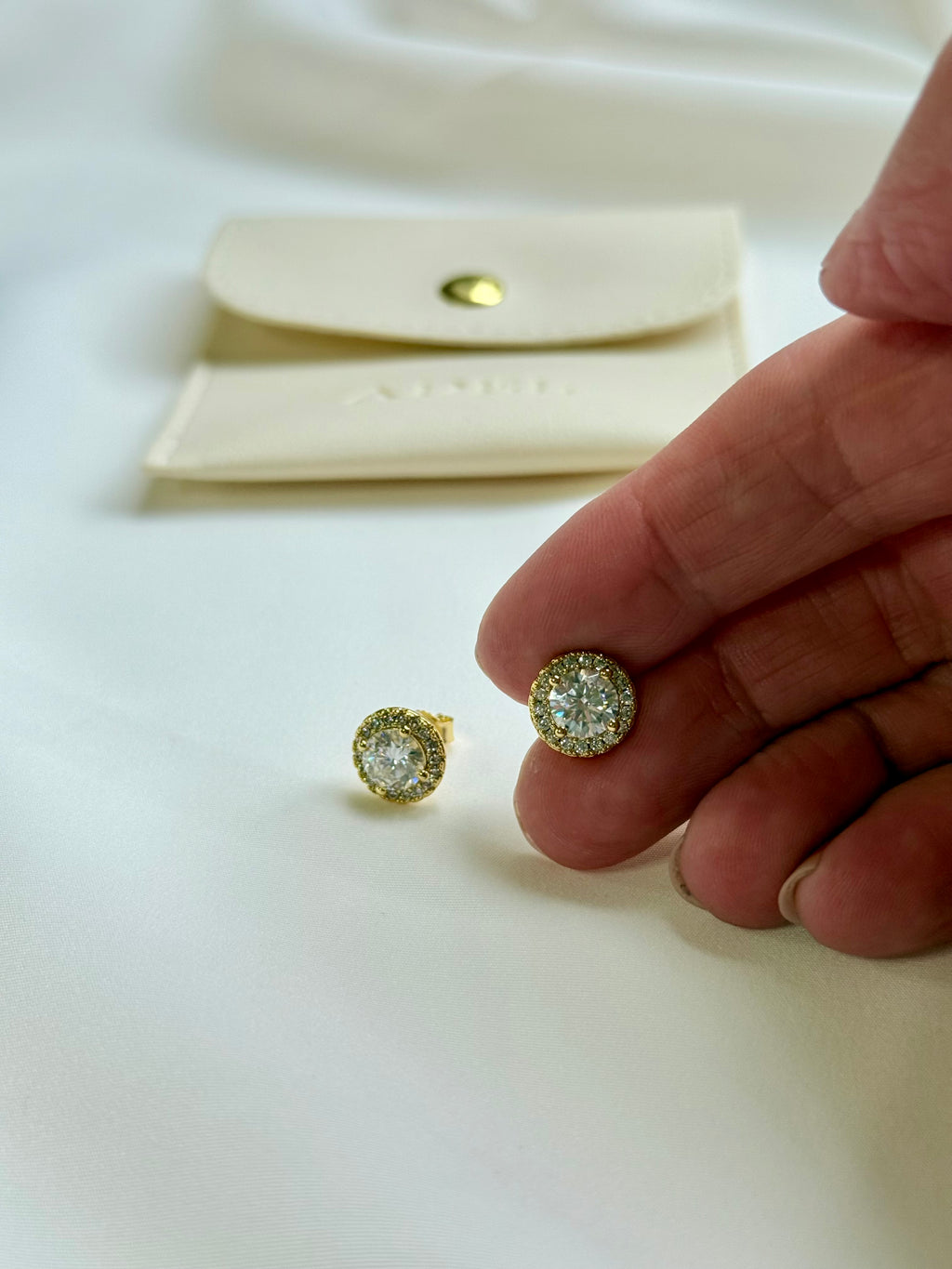 Gold and diamond earrings on a white surface with a hand holding one earring.
