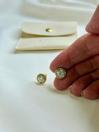 Gold and diamond earrings on a white surface with a hand holding one earring.