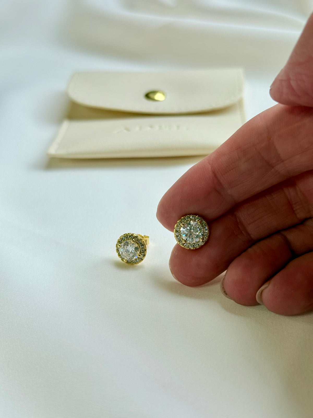 Gold and diamond earrings on a white surface with a hand holding one earring.