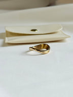 Gold ring on a white surface with a beige pouch in the background