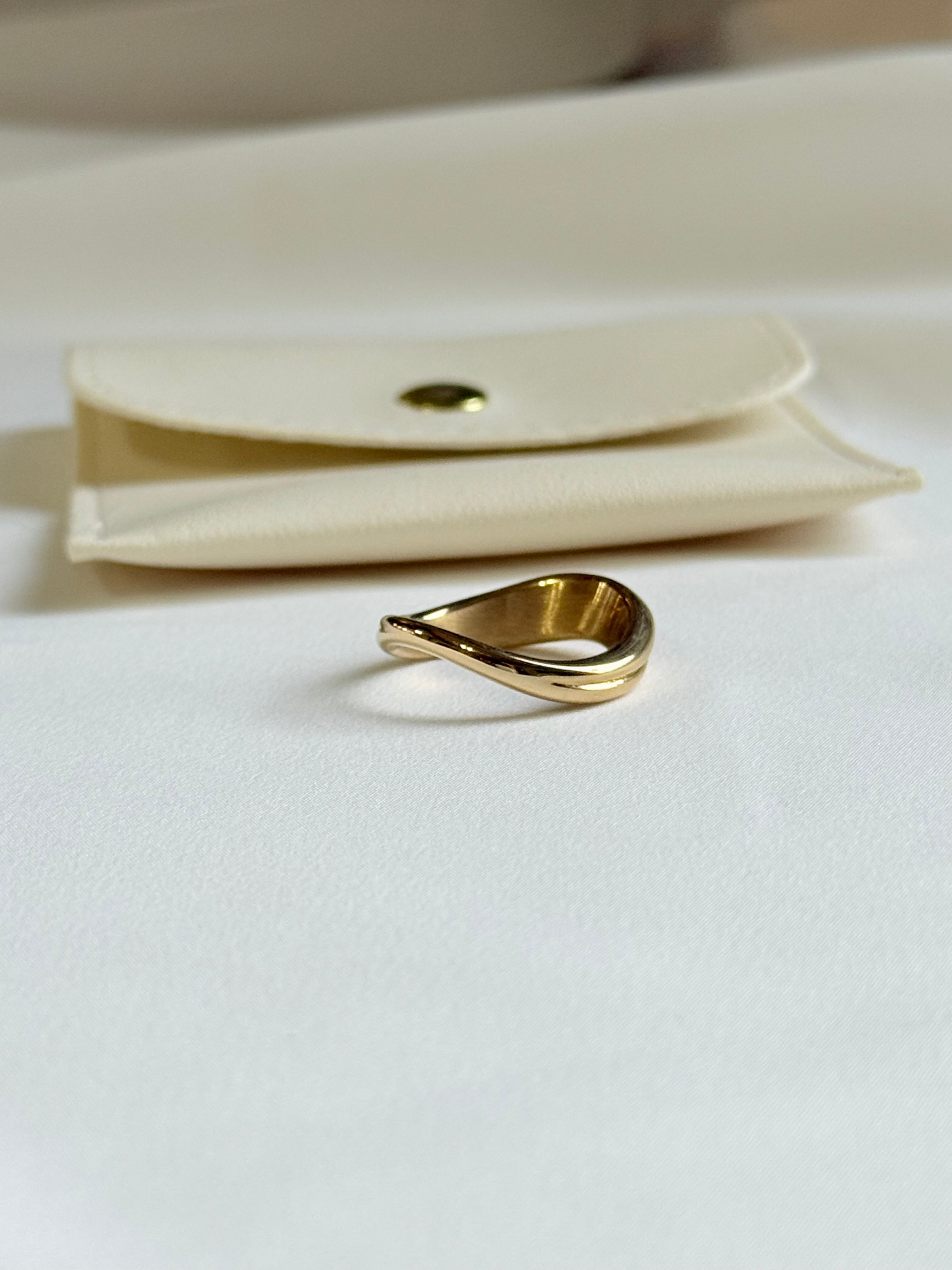 Gold ring on a white surface with a beige pouch in the background