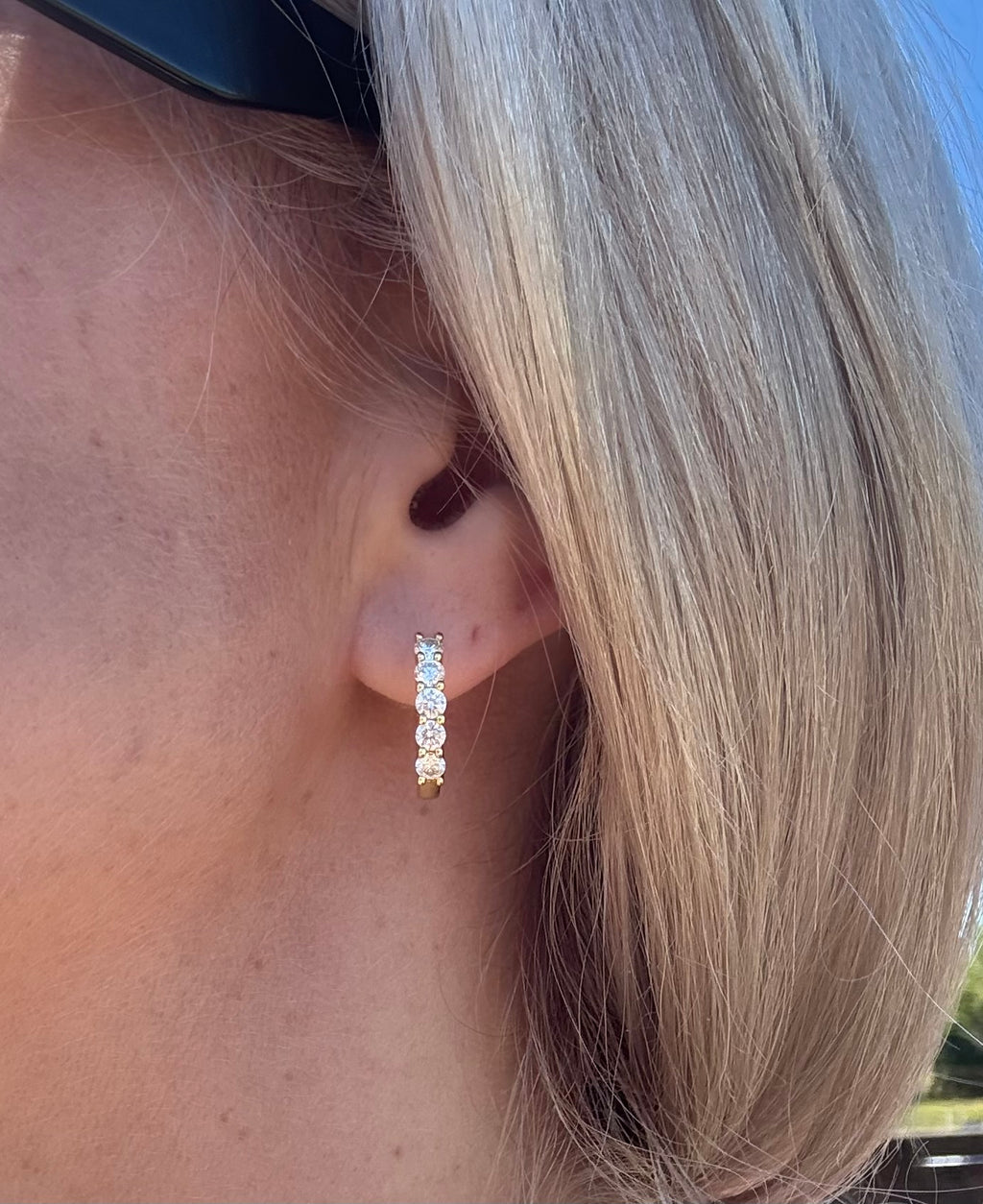 Close-up of an ear wearing a diamond hoop earring with blonde hair.