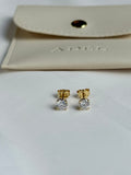 Gold and diamond stud earrings on a light gray surface with a beige pouch in the background.
