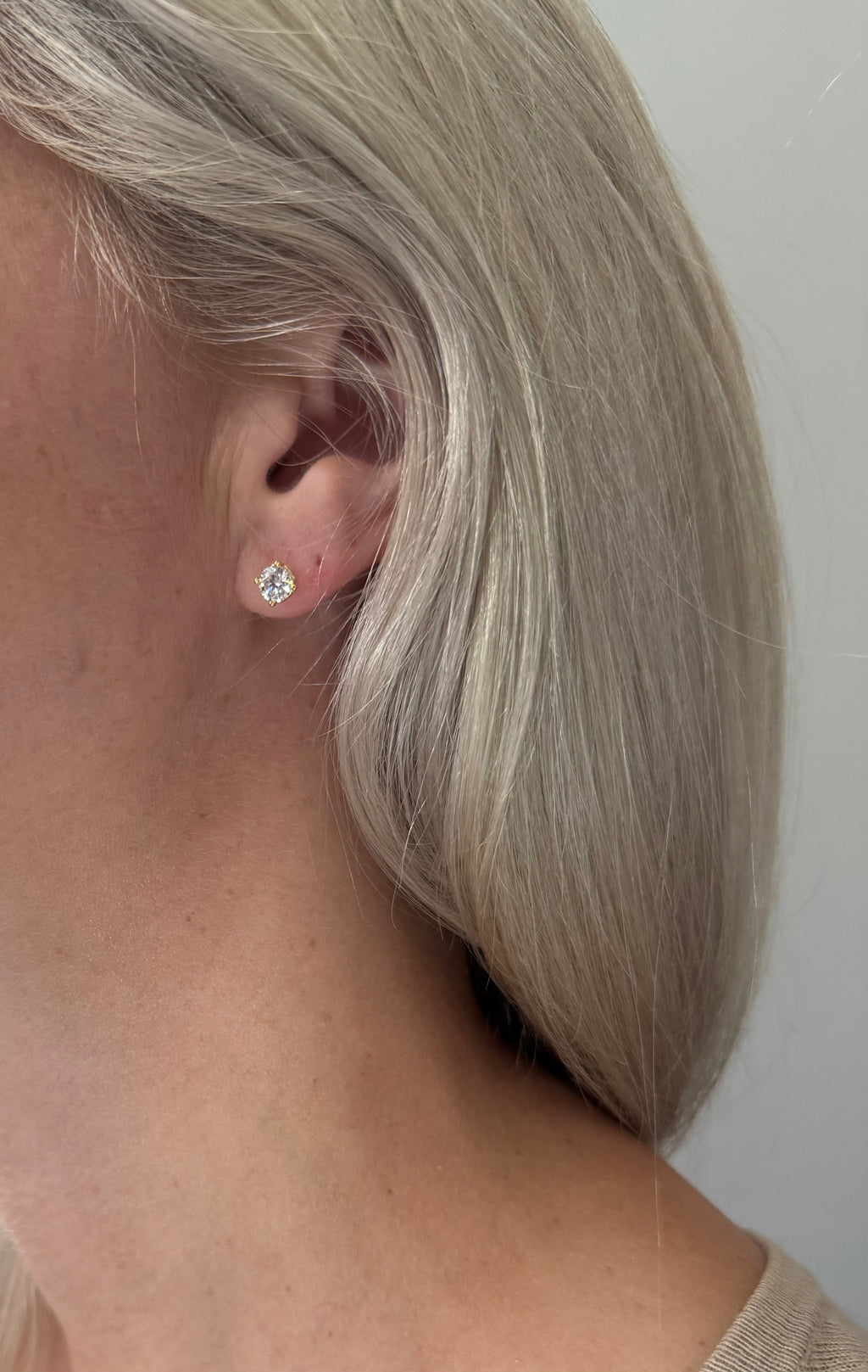 Close-up of an ear wearing a diamond earring with a plain background