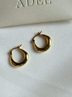 Gold hoop earrings on a white surface with 'ADEL' branding in the background.