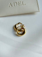 Gold hoop earrings on a white surface with 'ADEL' branding in the background.