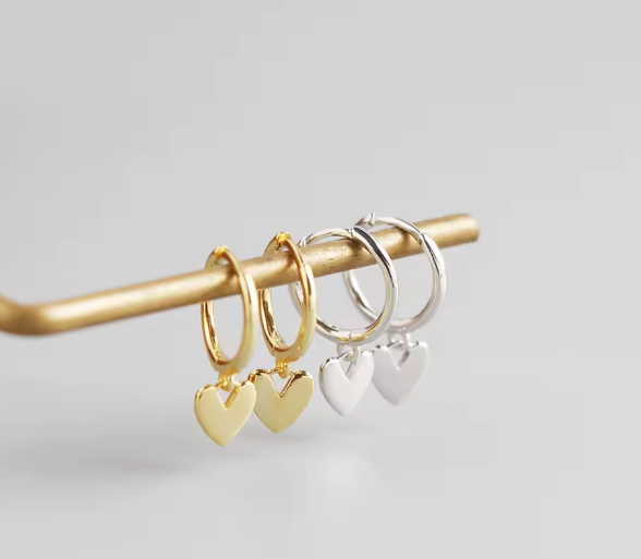 Two gold hoop earrings with heart charms on a gray background