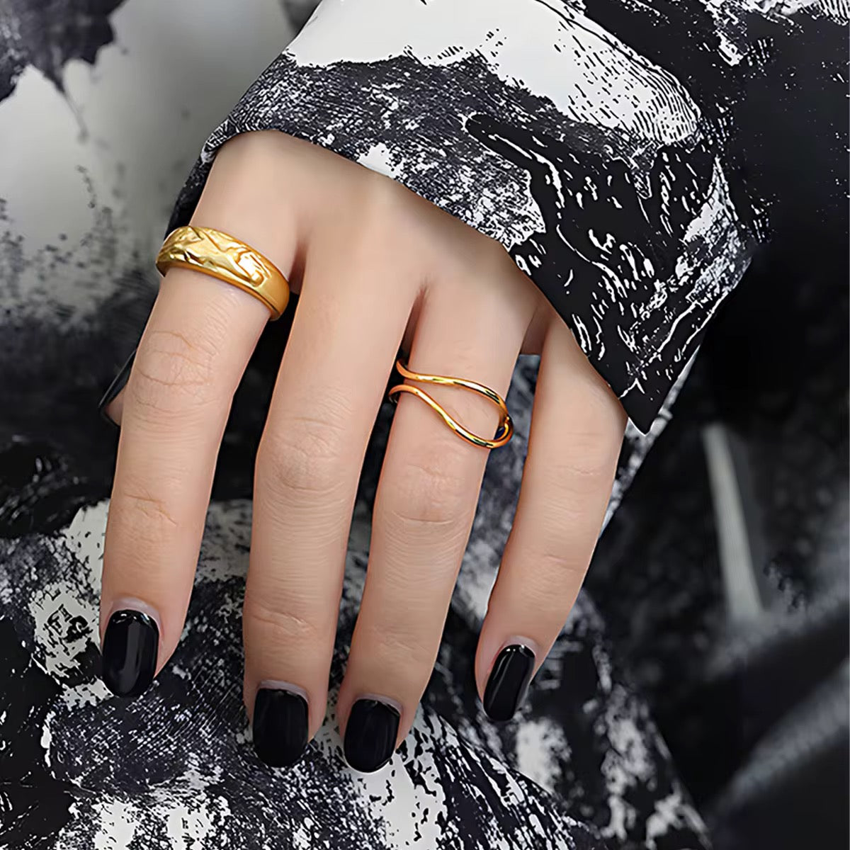 Close-up of a hand wearing two gold rings with black nail polish on a textured background