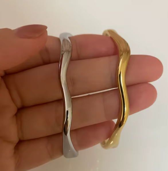 Gold and silver wavy bangles held in a hand against a white background