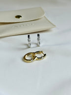 Gold and silver hoop earrings on a white surface with a beige pouch in the background.
