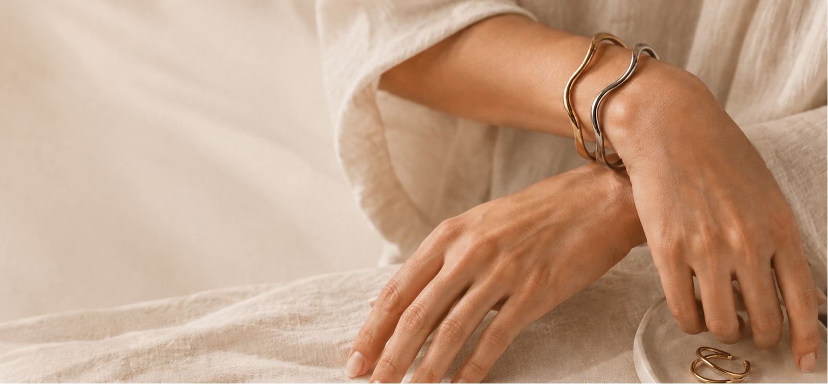 Close-up of a person's hands wearing gold bracelets on a neutral background