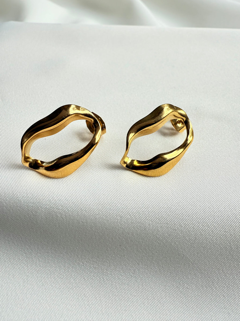Gold hoop earrings on a white satin background
