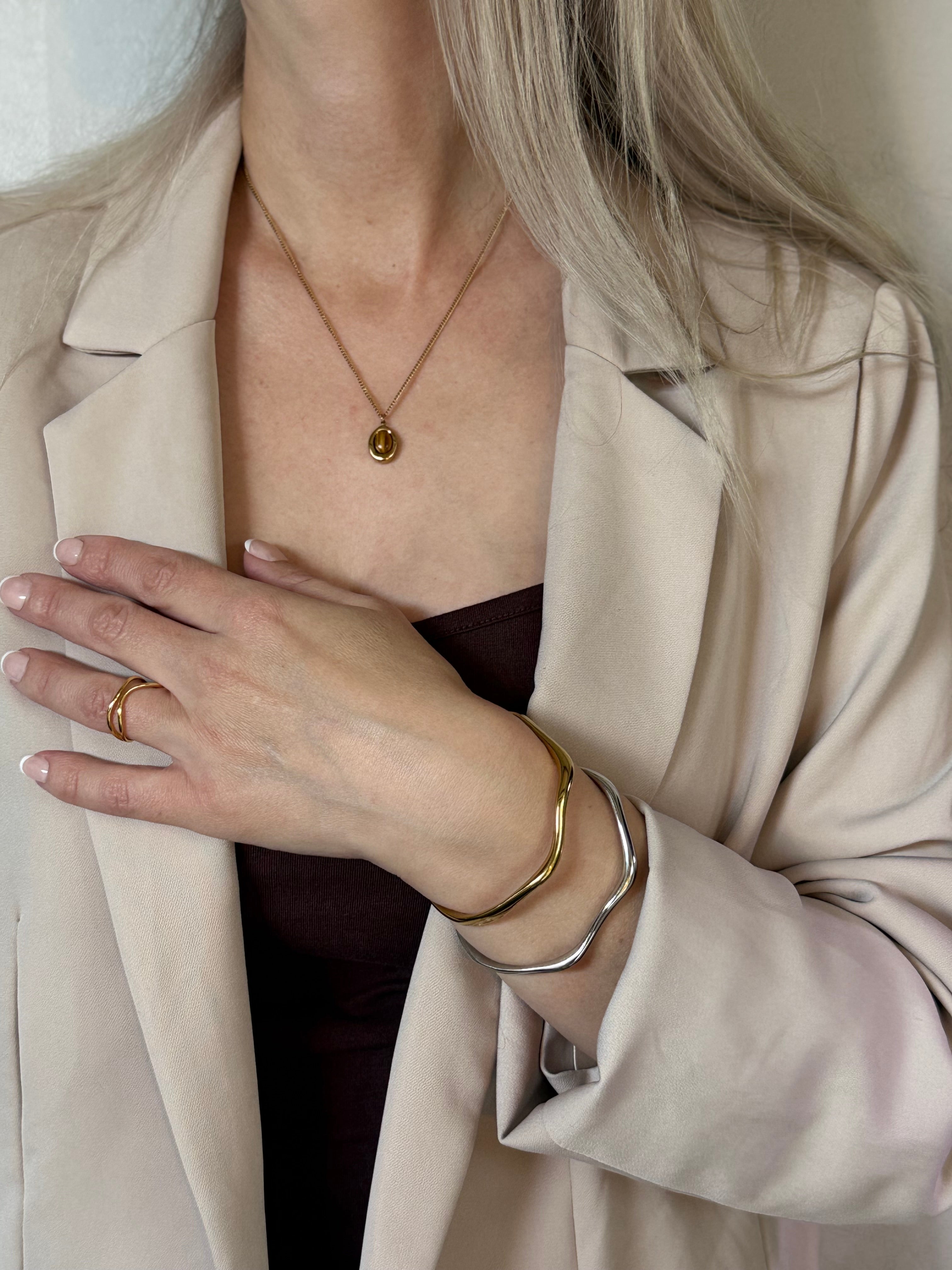 Person wearing a beige coat with jewelry including a necklace, ring, and bracelets.