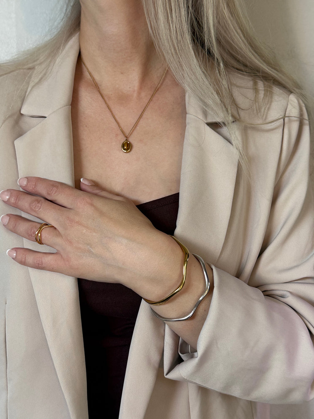 Person wearing a beige coat with jewelry including a necklace, ring, and bracelets.