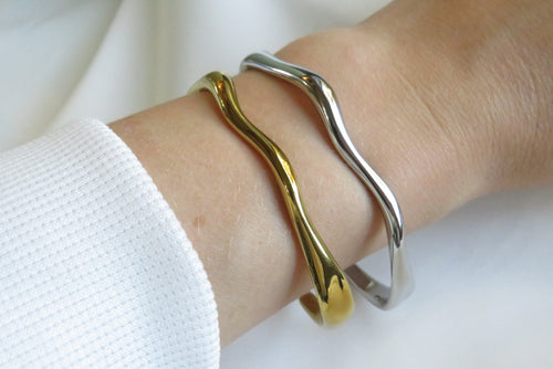 Gold and silver wave-patterned bracelets on a wrist against a white background