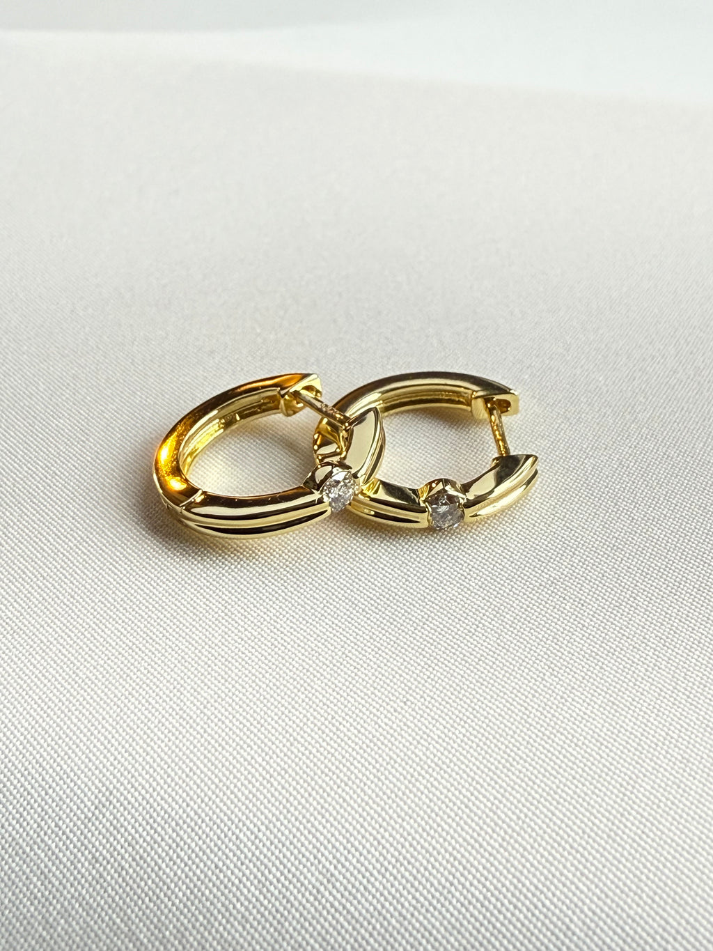 Gold hoop earring with small diamonds on a light gray background