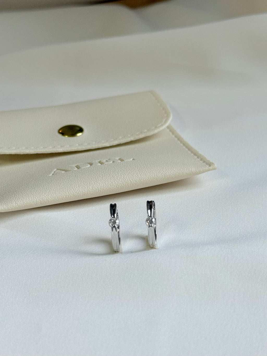 Silver earrings on a white surface with a beige jewelry pouch in the background.