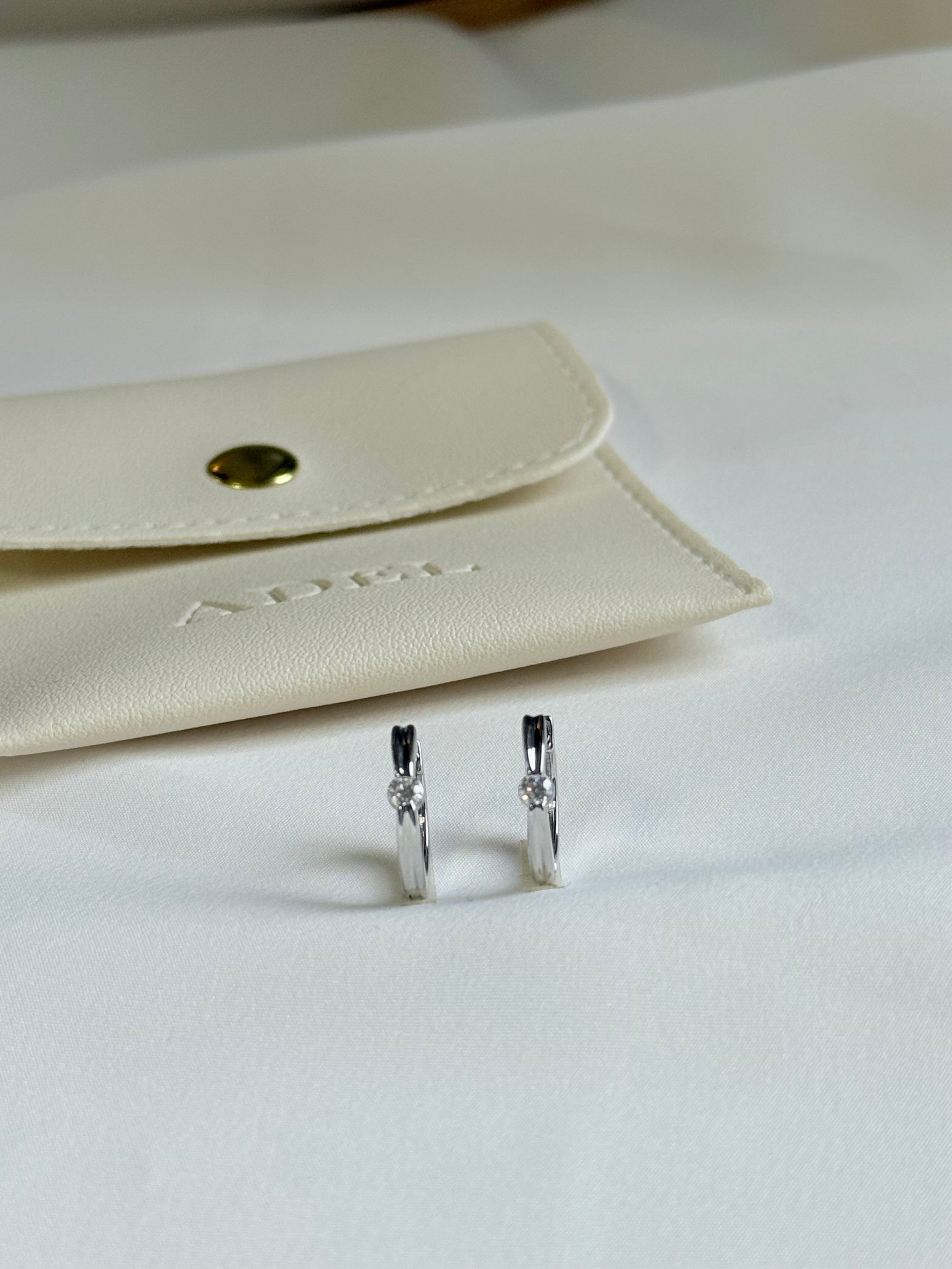 Silver earrings on a white surface with a beige jewelry pouch in the background.