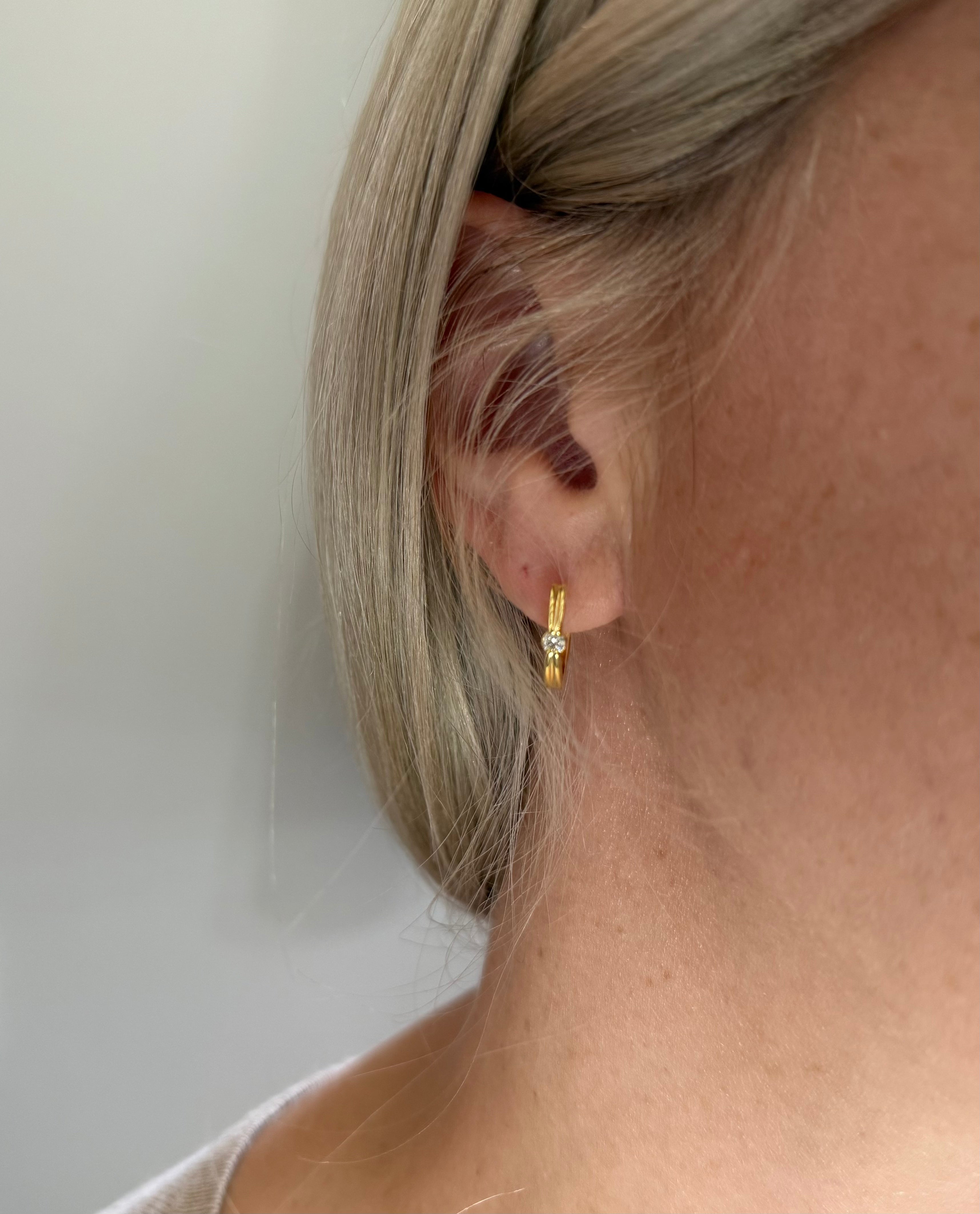 Gold hoop earring worn by a person with blonde hair against a neutral background