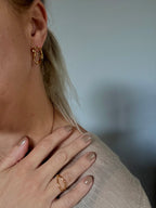 Close-up of a person wearing gold hoop earrings and a ring, with a blurred background.