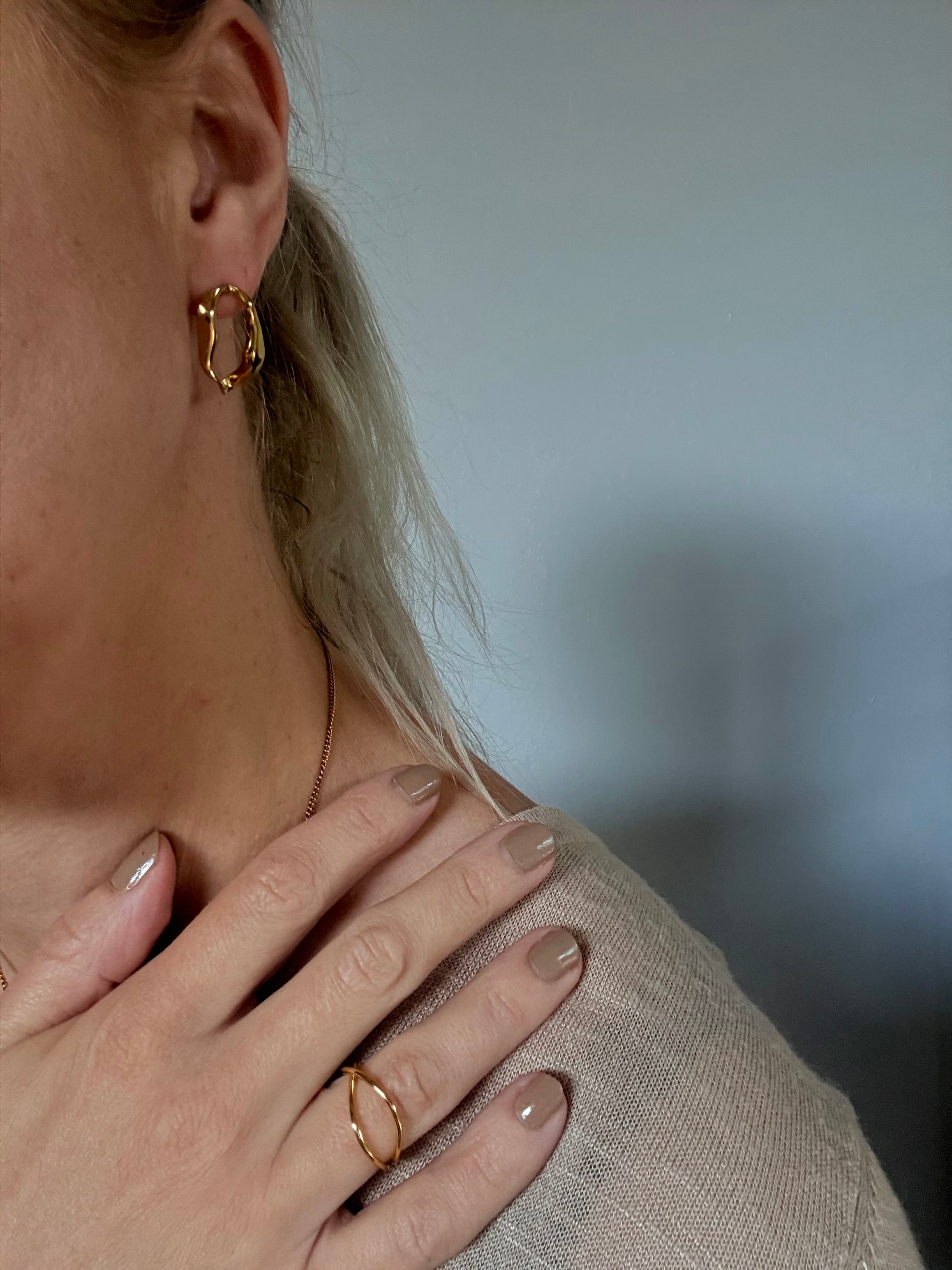 Close-up of a person wearing gold hoop earrings and a ring, with a blurred background.