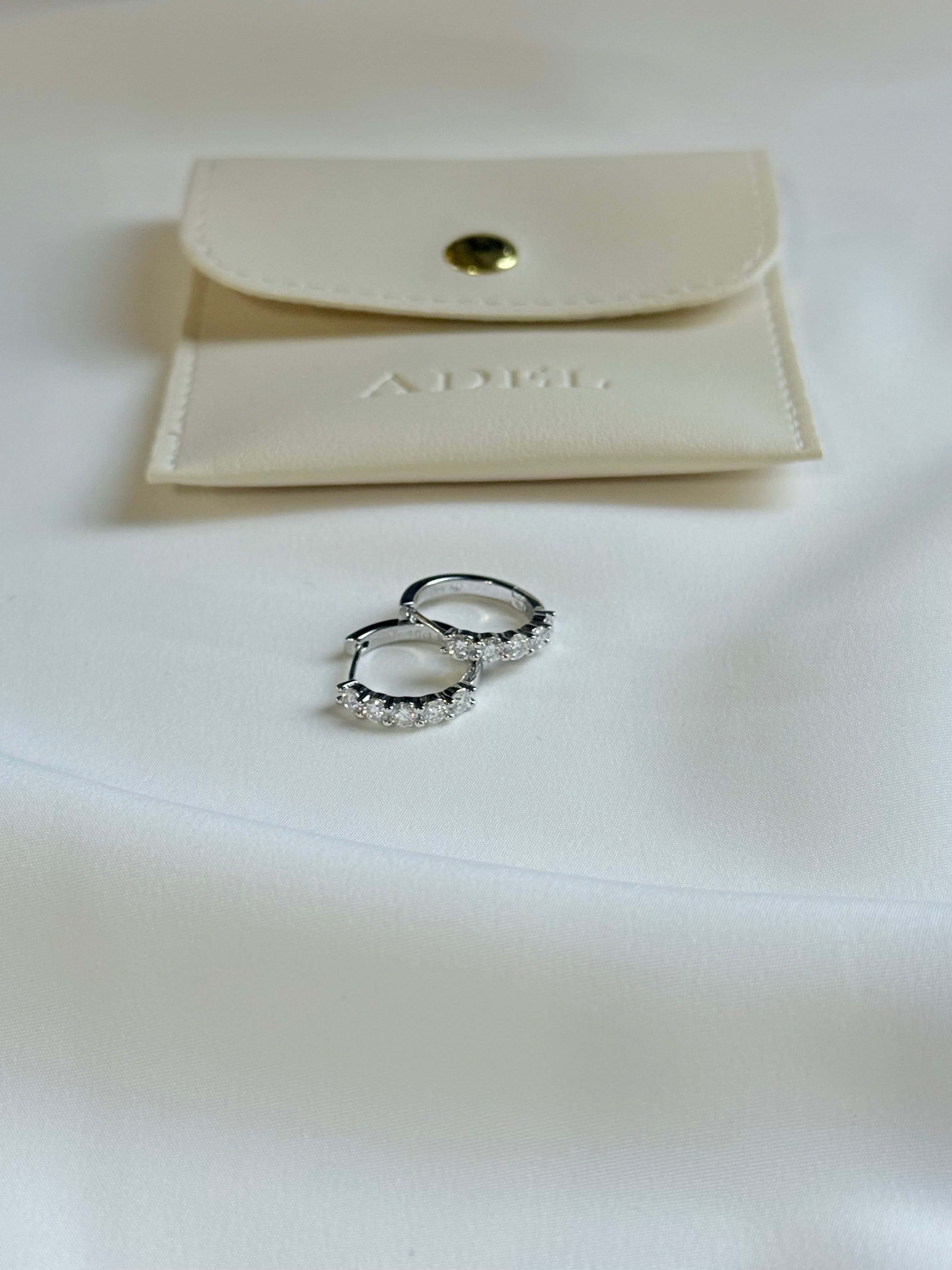 Pair of silver hoop earrings on a white surface with a beige jewelry pouch in the background.