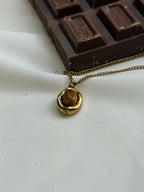 Gold necklace with a pendant next to a chocolate bar on a light fabric background