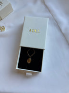 Gold necklace in an 'ADEL' branded box on a white background