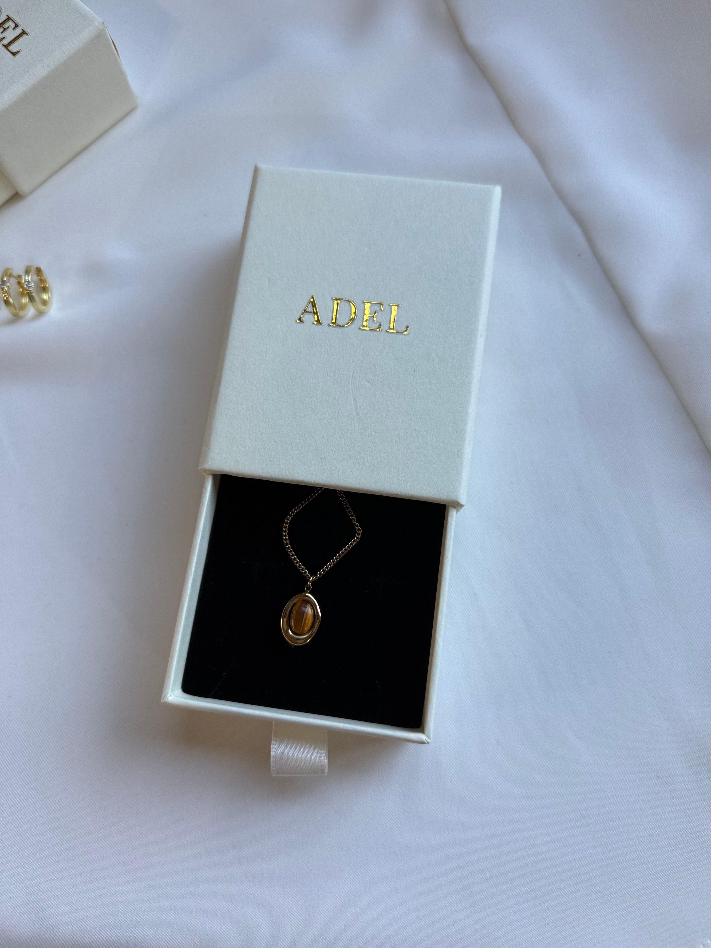 Gold necklace in an 'ADEL' branded box on a white background