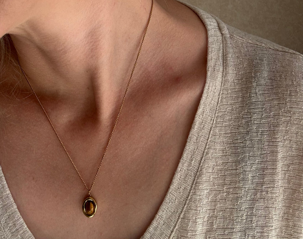Close-up of a necklace with an oval pendant on a neutral background