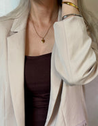 Person wearing a beige blazer over a dark top with a necklace and bracelet.
