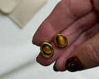 Gold earrings held between fingers with a blurred background