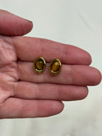 Gold earrings with amber stones held in a hand against a white background